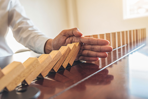 A hand stopping wooden blocks from falling like dominos