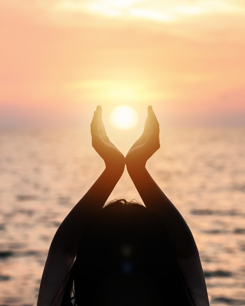 Woman framing setting sun with her hands looking over the ocean