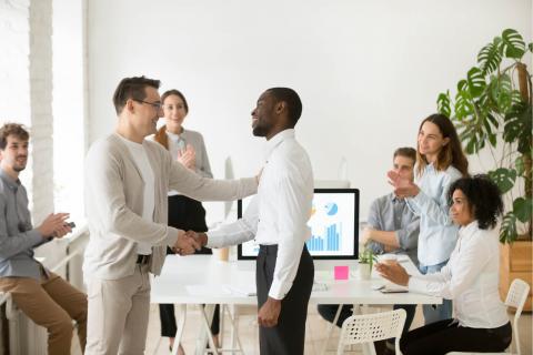 group of office workers welcoming a man with handshakes