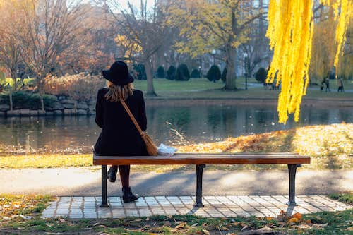 Woman sitting on a bench, facing away, looking at a pond in Fall